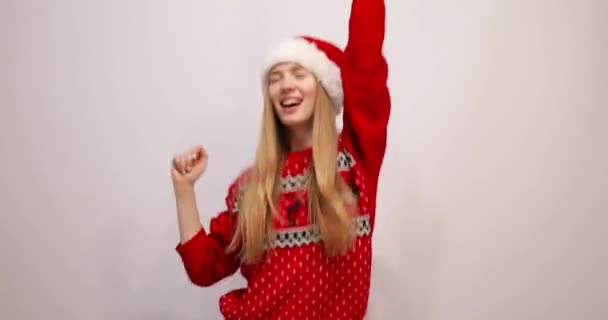 Podekscytowana radosną młodą kobietą noszącą świąteczny sweter i kapelusz Świętego Mikołaja, bawiącą się i tańczącą na białym tle, świętującą Nowy Rok — Wideo stockowe