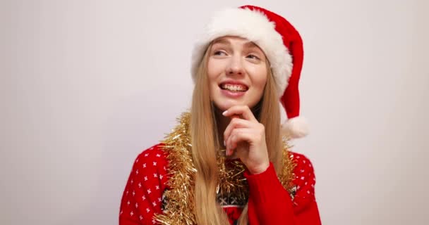 Soñando mujer joven en suéter de Navidad y sombrero de Santa Claus, sobre fondo blanco, celebrando el año nuevo — Vídeo de stock