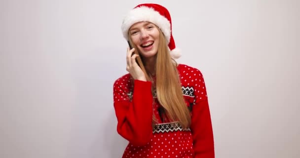 Vacker ung kvinna i jul Santa Claus hatt talar på mobiltelefon på vit bakgrund — Stockvideo