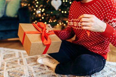 young man is holding a Christmas present with a red ribbon. Close-up, Gift opening
