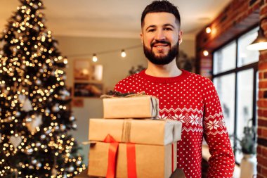 Happy young man in New Year's sweater, with many gift boxes at home, Merry Christmas