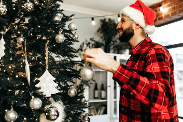 Young Happy Man Santa Claus Hat Decorates Christmas Tree Toys — Fotografia de Stock