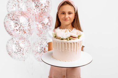 Güzel mutlu küçük kız elinde kocaman bir doğum günü pastası, balonlarla doğum günü kutlaması, izole edilmiş beyaz arka plan.