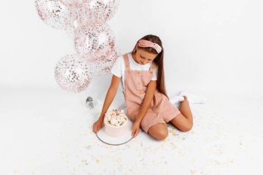 Balonlu ve büyük pastalı neşeli güzel çocuk doğum gününü kutluyor izole beyaz arka planda oturuyor.