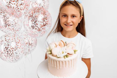 Güzel mutlu küçük kız elinde kocaman bir doğum günü pastası, balonlarla doğum günü kutlaması, izole edilmiş beyaz arka plan.