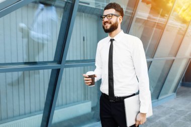 Başarılı bir iş adamı dizüstü bilgisayarla işe giderken elinde bir bardak sıcak içecek tutuyor.