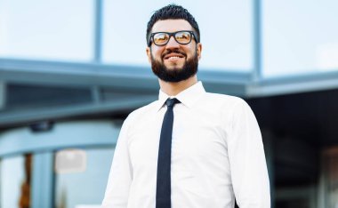 Ofis binasının arka planında kollarını kavuşturarak duran başarılı bir iş adamı.