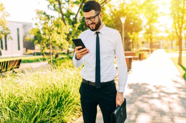 Gözlüklü mutlu iş adamı şehirde yürürken cep telefonu kullanıyor.