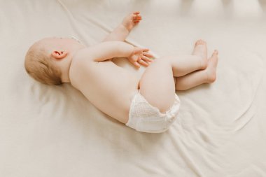 Bebek bezli şirin çocuk beyaz çarşafta uyuyor, küçük bebek evde uyuyor.