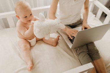 Genç bir kadın evde çalışmak ve küçük çocuğuyla oturmak için dizüstü bilgisayar kullanıyor.