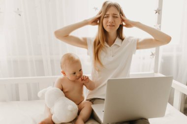 Sinirli anne dizüstü bilgisayar kullanıyor. Evde yaramaz küçük çocukla çalışıyor. Baş ağrısı çeken bir kadın.
