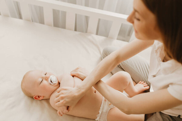 Mom massages newborn baby, gymnastics, physical fitness, strengthening exercises for babies, early development, health care concept