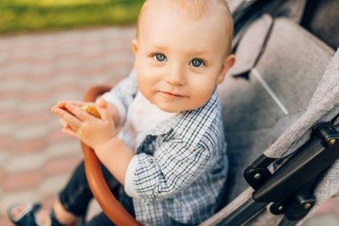 Küçük bir çocuk parkta bir bebek arabasında oturur ve annesini bekler.