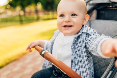 Küçük bir çocuk parkta bir bebek arabasında oturur ve annesini bekler.