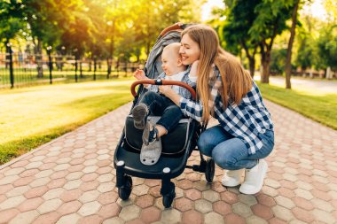Genç, güzel bir anne, küçük tatlı çocuğuyla güneşli bir yaz gününde parkta yürüyor..