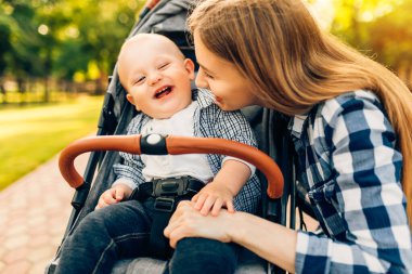 Güneşli bir günde parkta bebeğini öpen ve kucaklayan mutlu bir anne. Anneler Günü.,