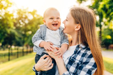 Güneşli bir günde, Anneler Günü 'nde parkta yürüyen ve bebeğine sarılan mutlu bir anne.,