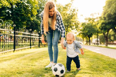 Mutlu genç anne ve küçük oğlu parkta birlikte futbol oynuyorlar.