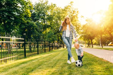 Mutlu genç anne ve küçük oğlu parkta birlikte futbol oynuyorlar.