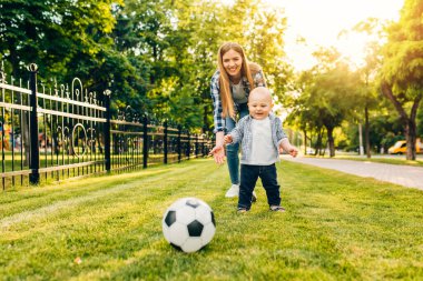 Mutlu genç anne ve küçük oğlu parkta birlikte futbol oynuyorlar.