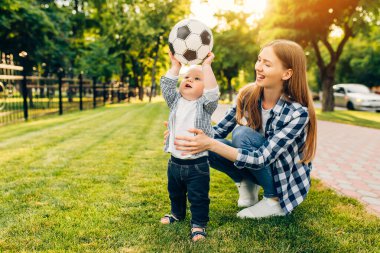 Mutlu genç anne ve küçük oğlu parkta birlikte futbol oynuyorlar.