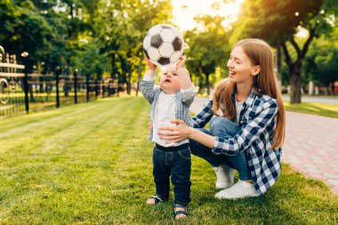 Mutlu genç anne ve küçük oğlu parkta birlikte futbol oynuyorlar.