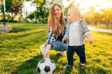 Mutlu aile dışarıda birlikte vakit geçiriyor. Anne ve küçük çocuk yeşil çimenlerde otururken eğleniyorlar.