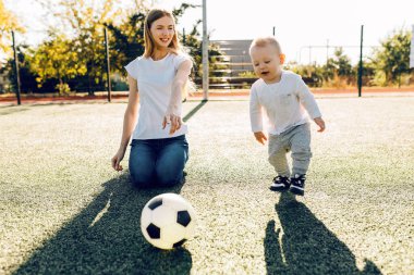 Sahada, dışarıda oğluyla futbol oynayan mutlu genç bir anne.
