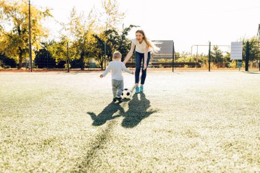 Sahada, dışarıda oğluyla futbol oynayan mutlu genç bir anne.