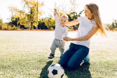 Sahada, dışarıda oğluyla futbol oynayan mutlu genç bir anne.