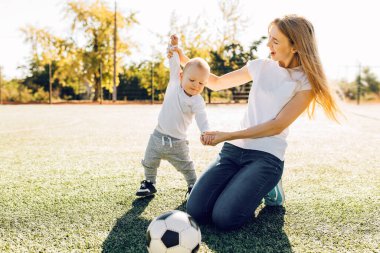 Sahada, dışarıda oğluyla futbol oynayan mutlu genç bir anne.