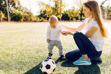 Mutlu genç anne ve oğlu sahada, dışarıda futbol oynuyorlar.
