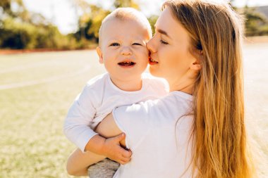 Mutlu anne, güneşli bir yaz gününde parkta bebeğini öper ve ona sarılır. Anneler gününde.