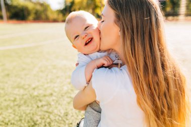 Mutlu anne, güneşli bir yaz gününde parkta bebeğini öper ve ona sarılır. Anneler gününde.