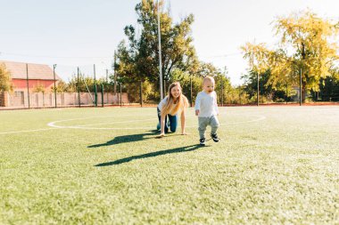 Mutlu anne ve küçük oğlu çimlerin üzerinde oynuyorlar, anne ve neşeli çocuğu parkta eğleniyorlar, mutlu bir ailenin portresi.