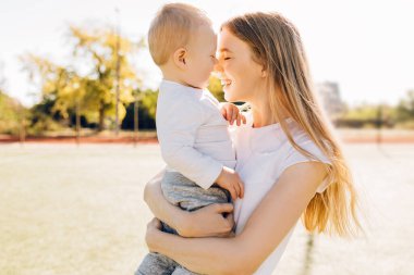 Bebekle ilgilenen genç bir anne, sevgi dolu bir anne küçük çocuğu öpüyor güneşli bir günde dışarıda şefkatli aile anlarının tadını çıkarıyor, Anneler Günü.