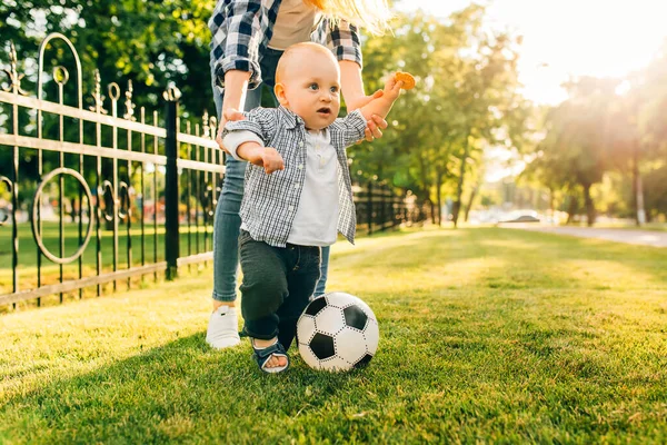 Happy young mom and her little son play soccer together outdoors in the park