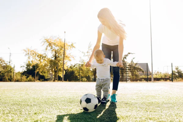 Happy young mom with son play soccer on the field, outdoors