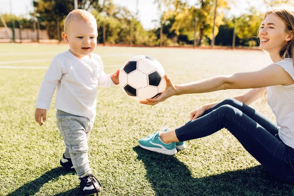 Happy young mom with son play soccer on the field, outdoors