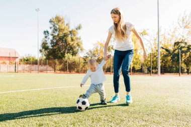 Mutlu genç anne ve oğlu sahada, dışarıda futbol oynuyorlar.