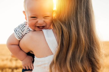 Mutlu bir aile, güzel, genç bir anne, bir elbisenin içinde, altın buğday tarlasında küçük bir bebekle yaz günü gün batımında.
