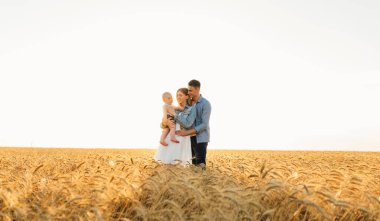 Mutlu aile gün batımında buğday tarlasında birlikte harika vakit geçiriyorlar.