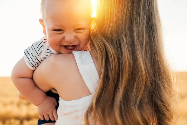 Mutlu bir aile, güzel, genç bir anne, bir elbisenin içinde, altın buğday tarlasında küçük bir bebekle yaz günü gün batımında.