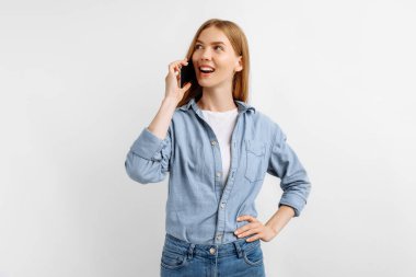 Güzel, mutlu, genç bir kadın cep telefonuyla konuşuyor ve beyaz arka planda yalnız başına gülüyor.