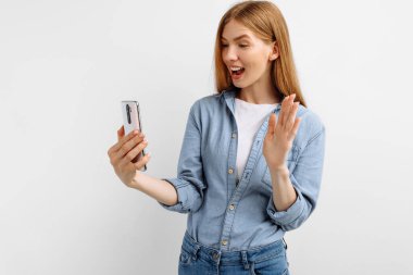 Güzel, mutlu, genç bir kadın beyaz arka planda izole edilmiş cep telefonuyla selfie çekiyor.