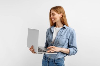 İzole edilmiş beyaz bir arka planda dizüstü bilgisayar kullanan neşeli bir genç kadın görüntüsü