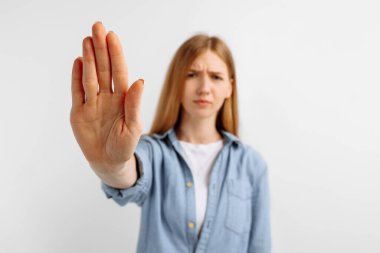 Ciddi genç bir kadının portresi, elini uzatmış, beyaz arka planda izole edilmiş dur hareketi sergiliyor.