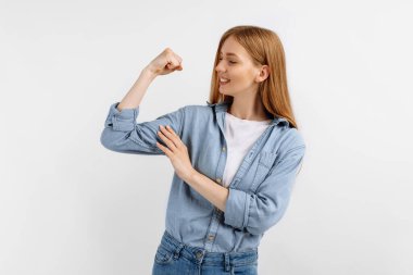 Güçlü genç kadın kollarını kaldırıp pazılarını gösteriyor. Beyaz arka plandaki kaslarıma bakın.