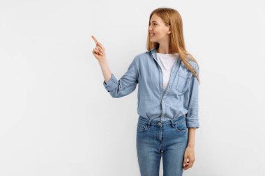 Heyecanlı genç kadın, beyaz arka planda tek başına dikilirken fotokopi uzayı işaret ediyor.