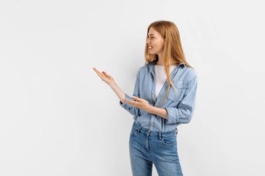 Heyecanlı genç kadın, beyaz arka planda tek başına dikilirken fotokopi uzayı işaret ediyor.